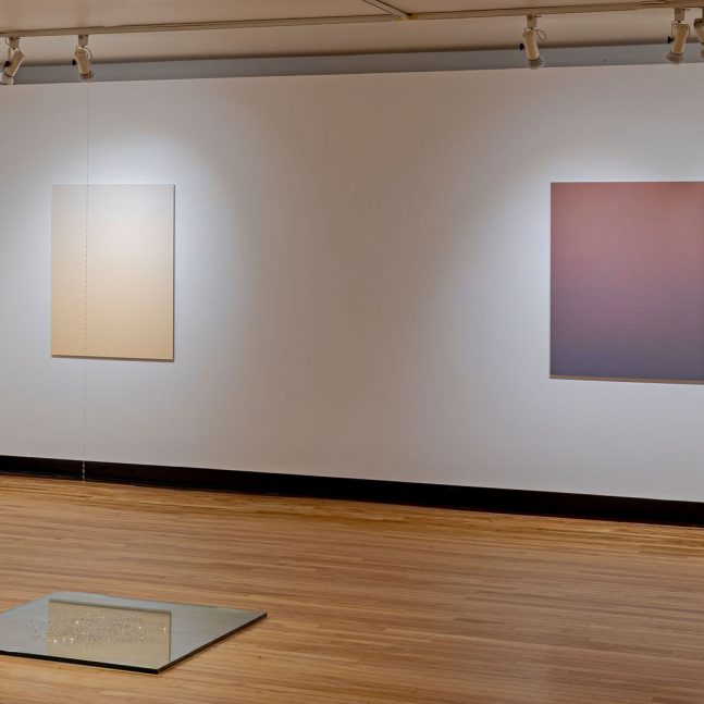 Four gradient images hang on the walls with a small square mirrored surface on the floor