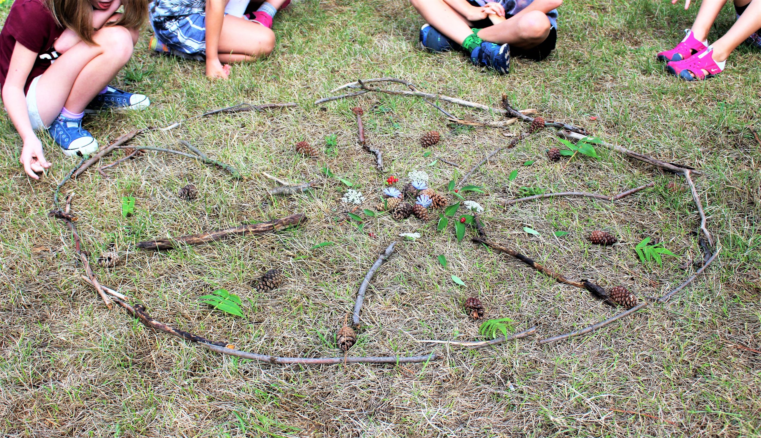 A photograph of four children gathered around a circle made of sticks and acorns.