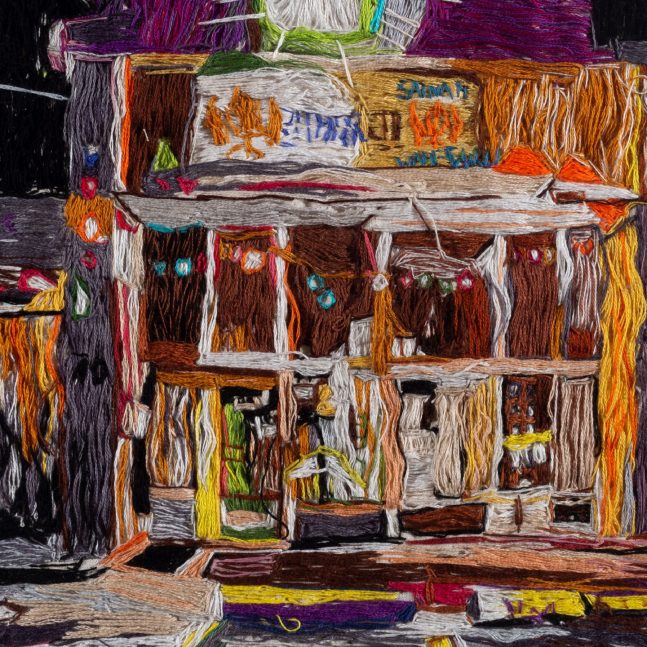 Colourful stitch art of a building with a dark background.