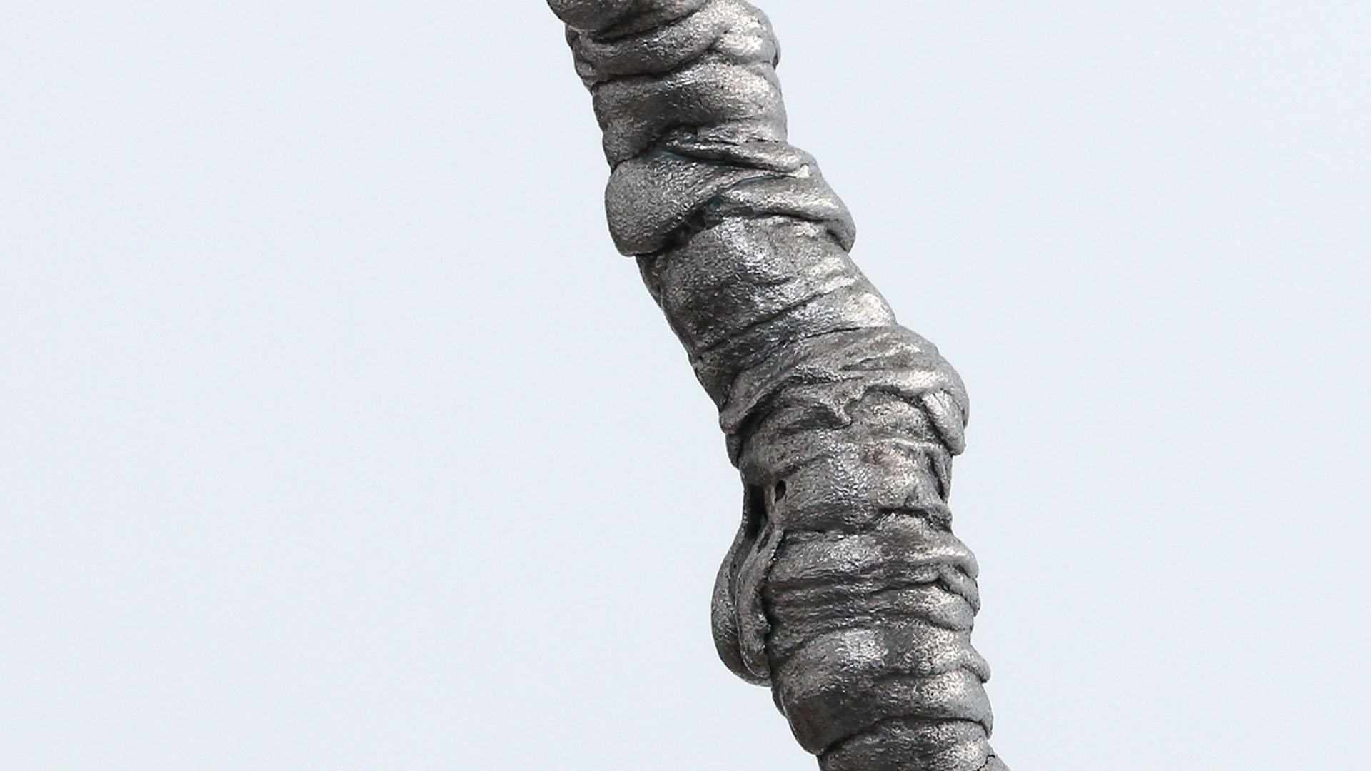 A photo of a grey viscous substance that is shaped into a vertical line, all surrounded by a white background.
