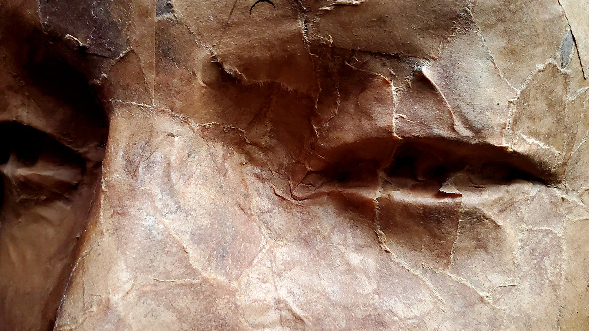 A close up photograph of a brown paper macheted face with multiple cracks.