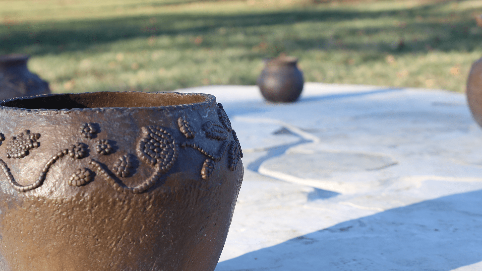 A photograph of four brown pots, with 3 being distant, and one close. The pot has patterns of leaves and flowers.