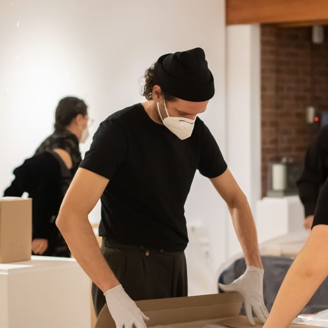 Person wearing a mask and latex gloves examines an object.