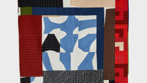 A textile artwork made up of abstract shapes in various shades of white, red, blue, brown, and green.