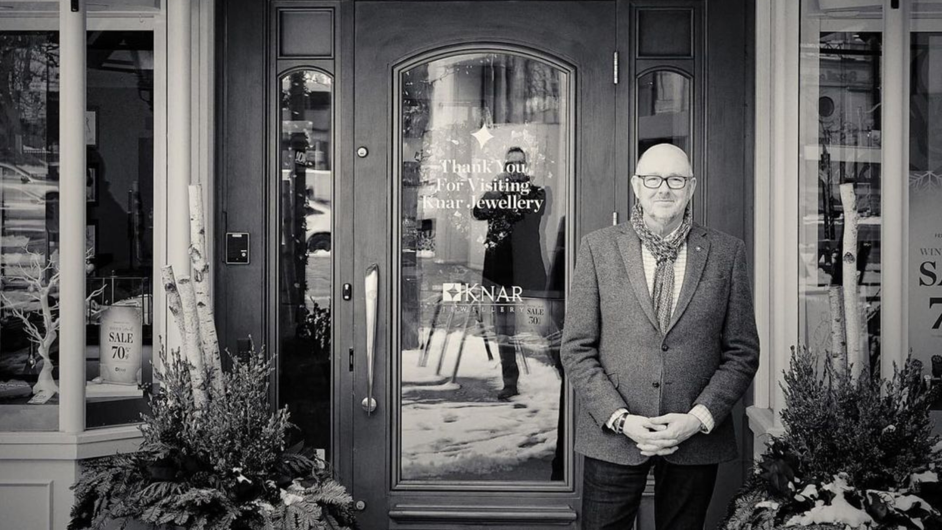 black and white photo showing a man wearing a suit standing outside Knar Jewellery shop