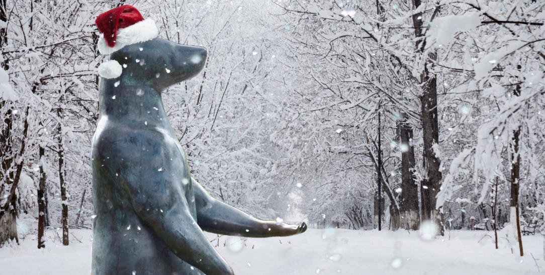 the Begging Bear sculpture wearing a santa hat in the snow